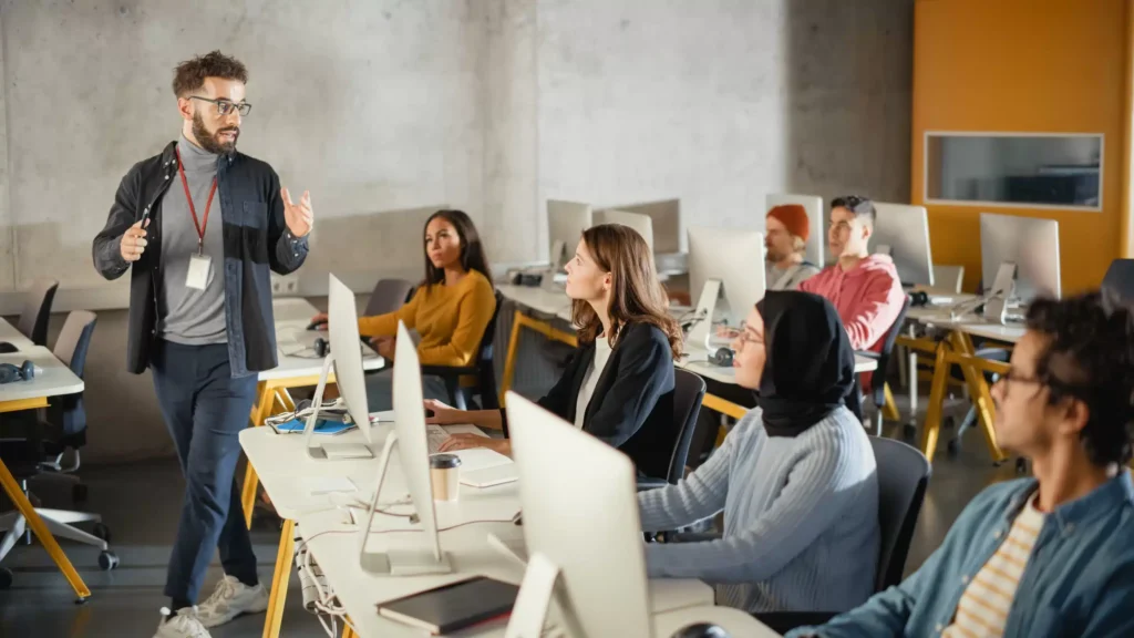 a man standing in front of a group of people in a room with computers