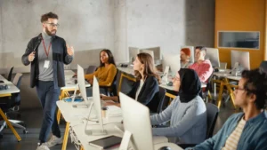 a man standing in front of a group of people in a room with computers