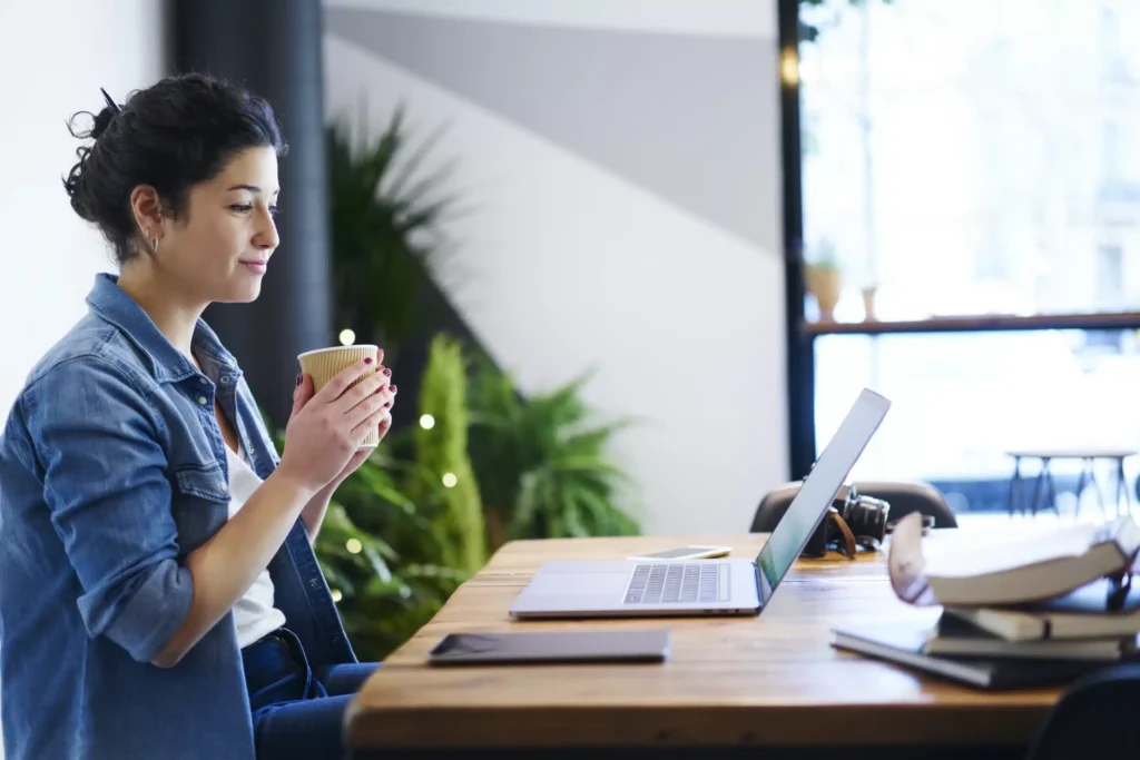 a woman holding a cup and looking at a laptop
