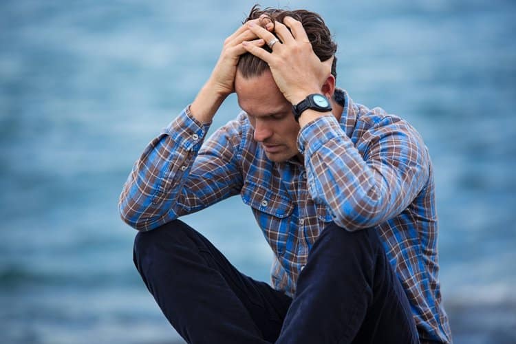 Troubled man cross sitting near water