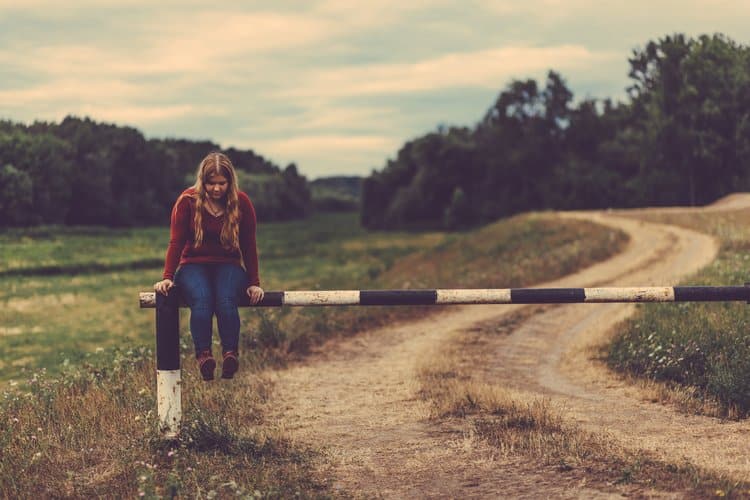 Sad teen sitting alone in a field near a road