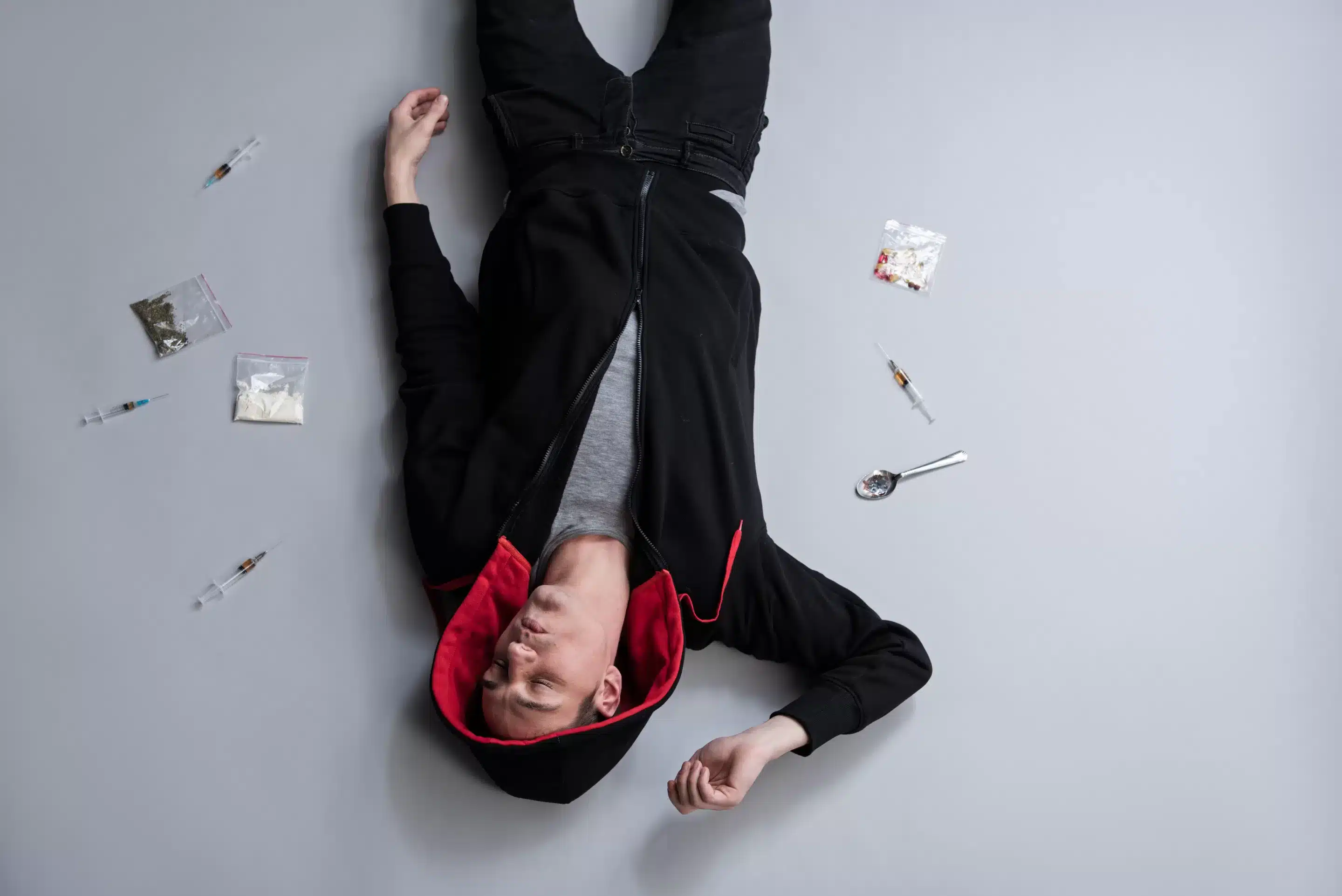 Despair concept. Overdosed young man and lot of narcotic lying on the floor. Top view