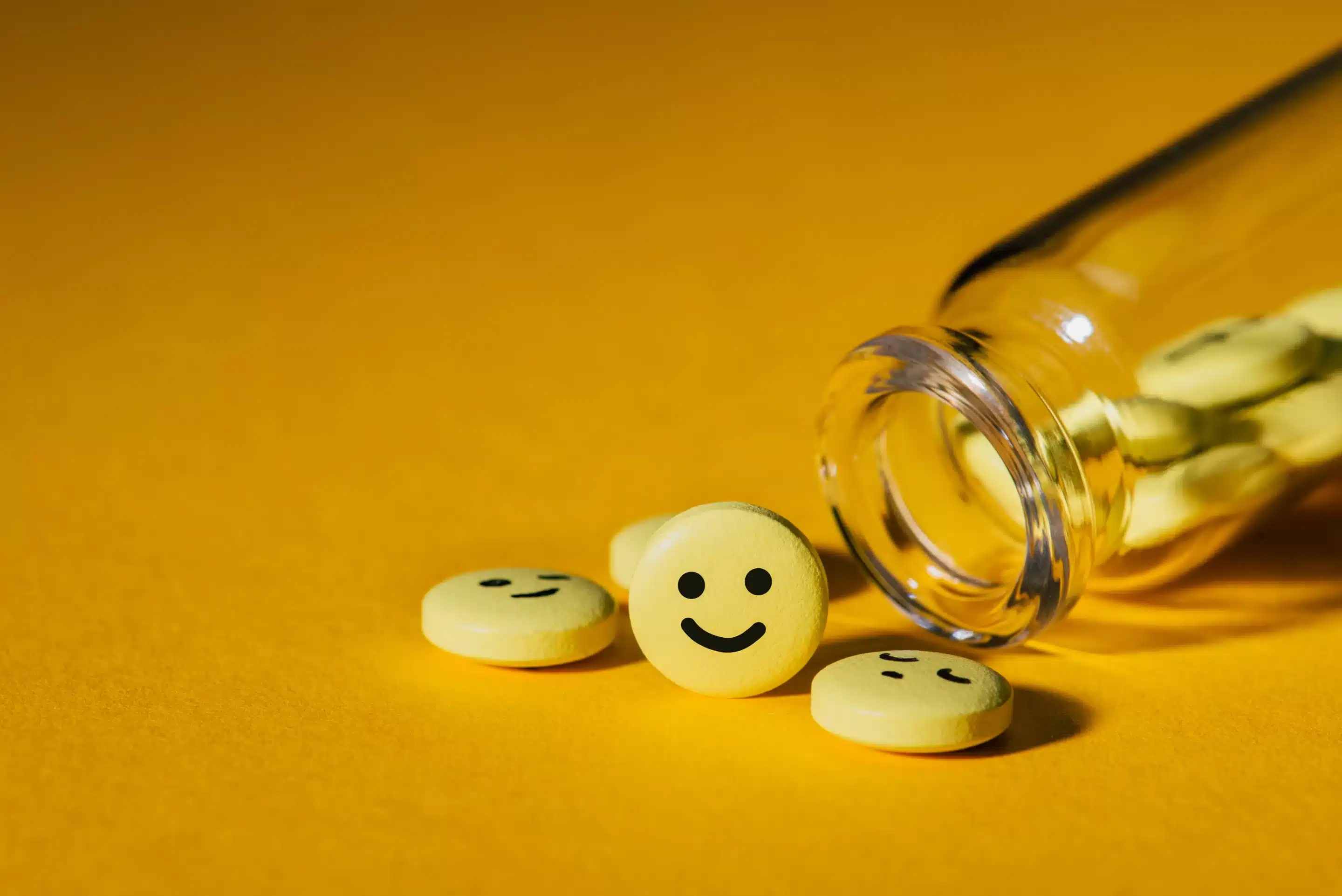 close-up shot of pills with smiley faces and glass bottle on yellow