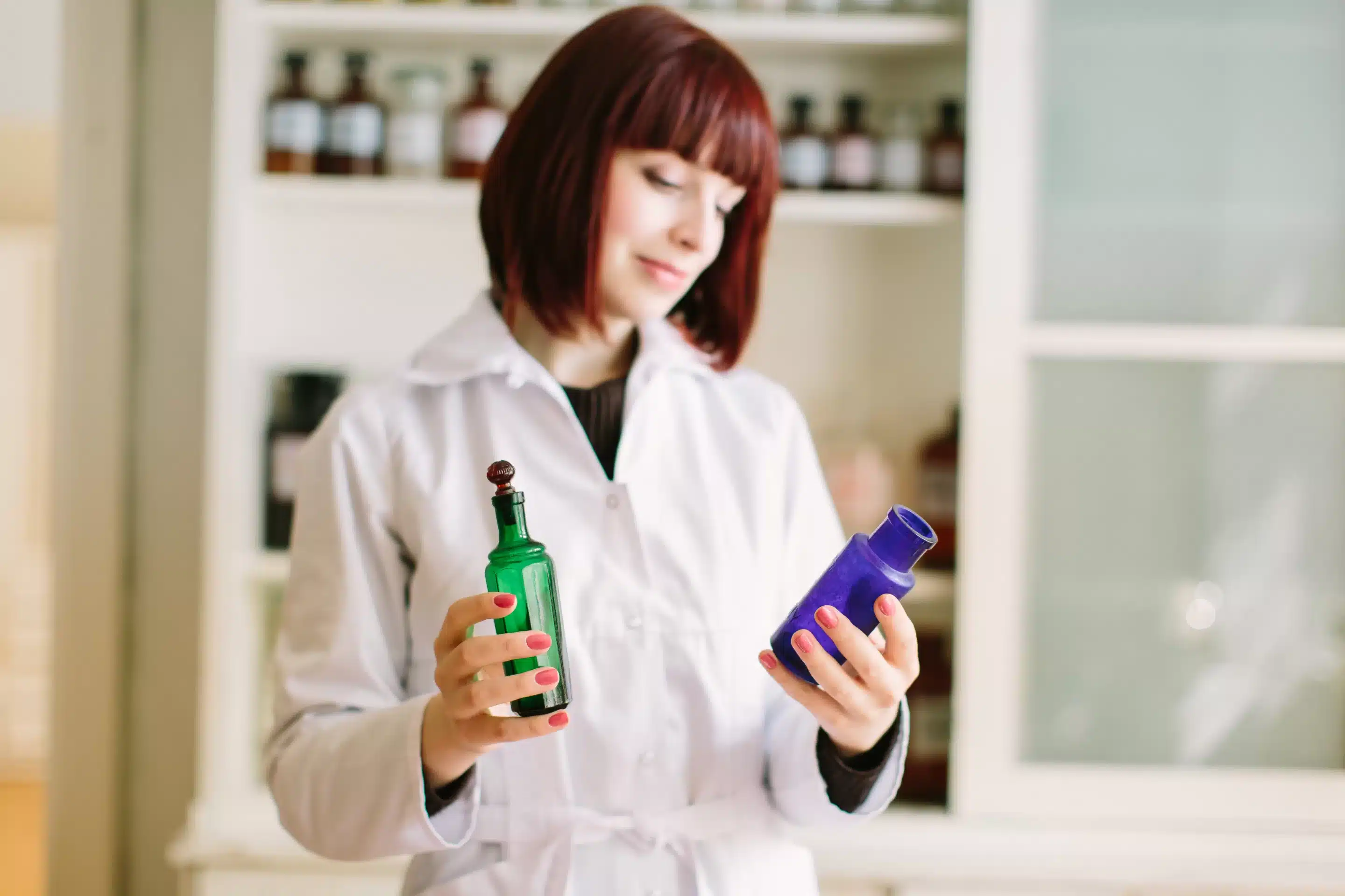 Smiling attractive young lady pharmacist holding green and blue glass