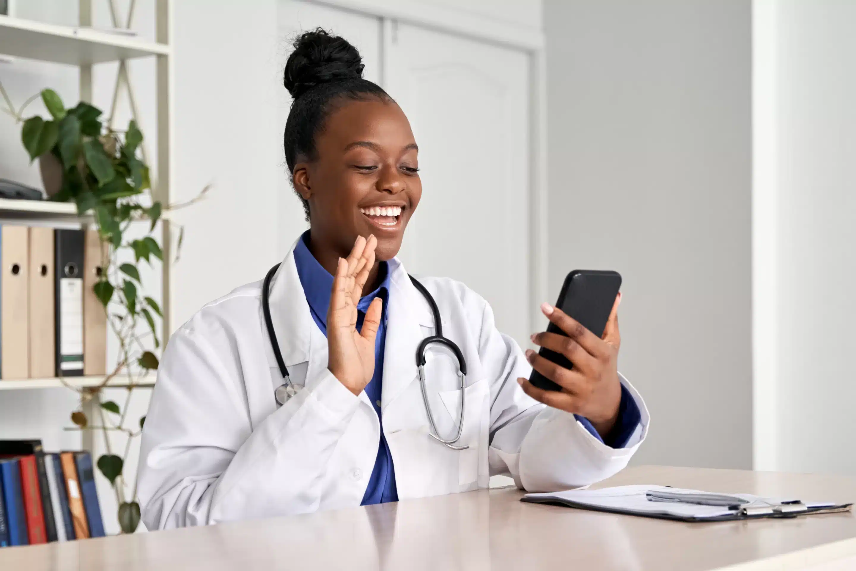 a woman in a white coat and stethoscope waving at a phone