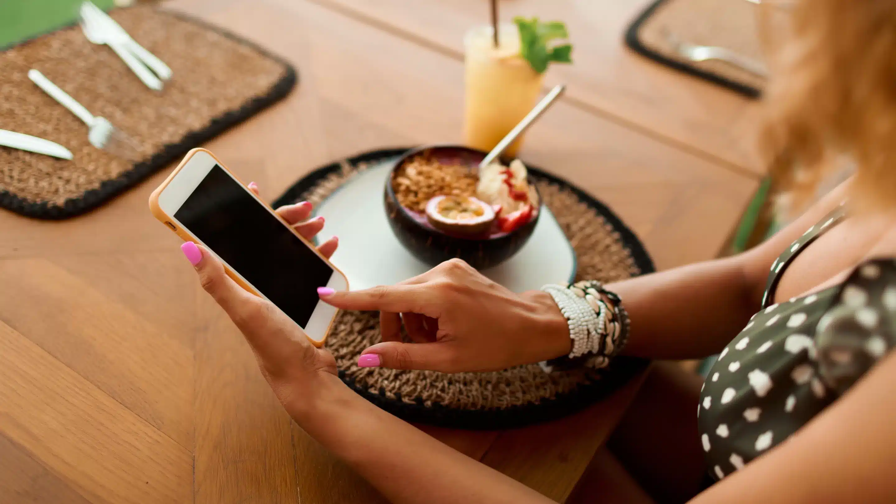 European woman using mobile phone in cafe. Enjoying tropical dish with passion