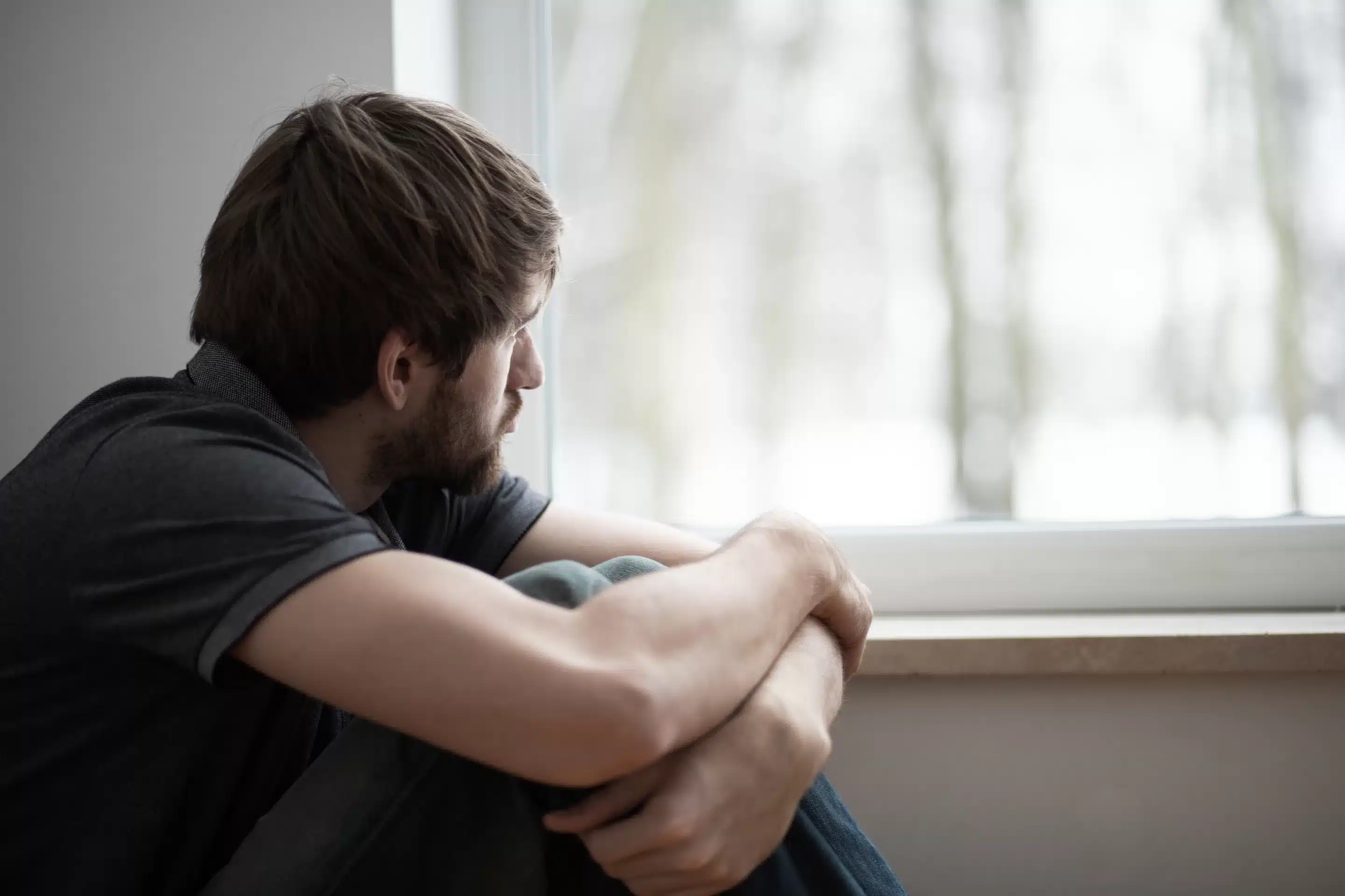 Ketamine Sad young man sitting on the floor looking through the window
