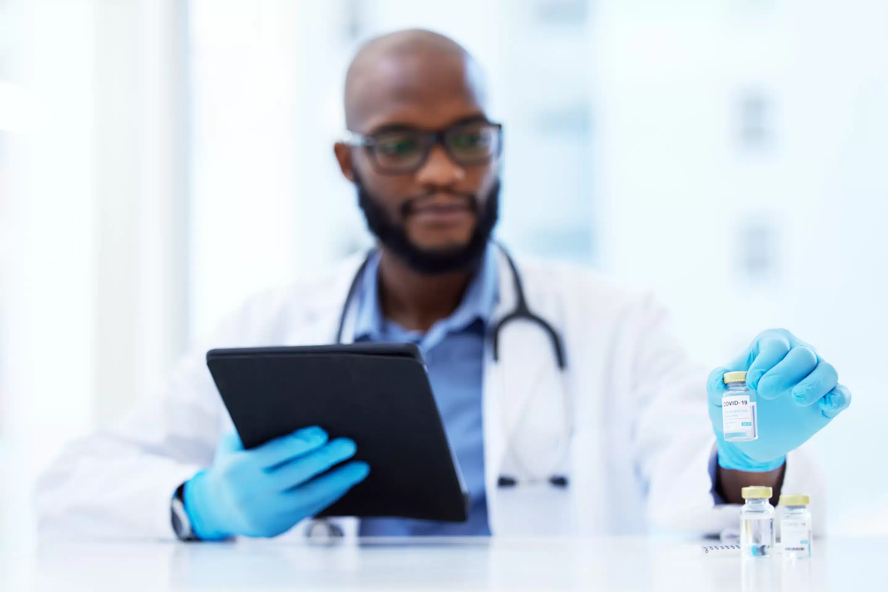 a man in a white coat and blue gloves holding a tablet
