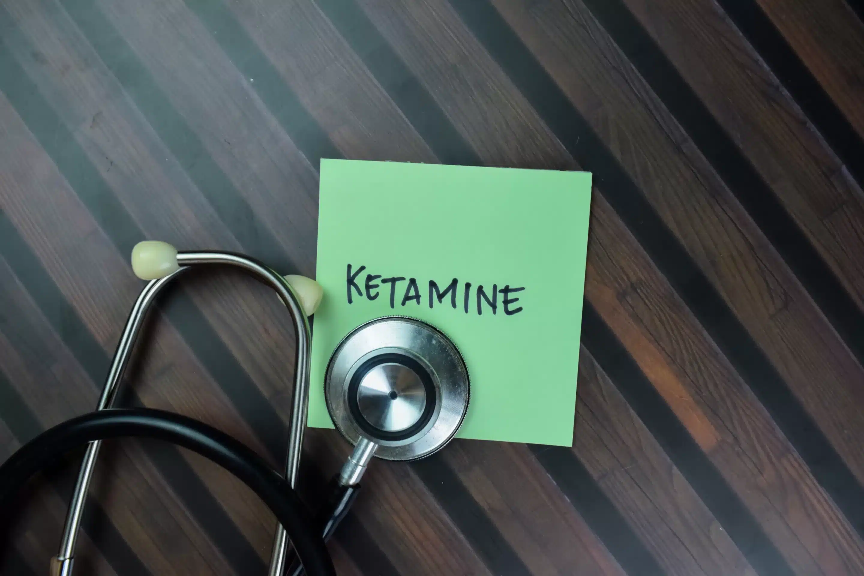 Ketamine Concept of Ketamine write on sticky with stethoscope notes isolated on Wooden Table.