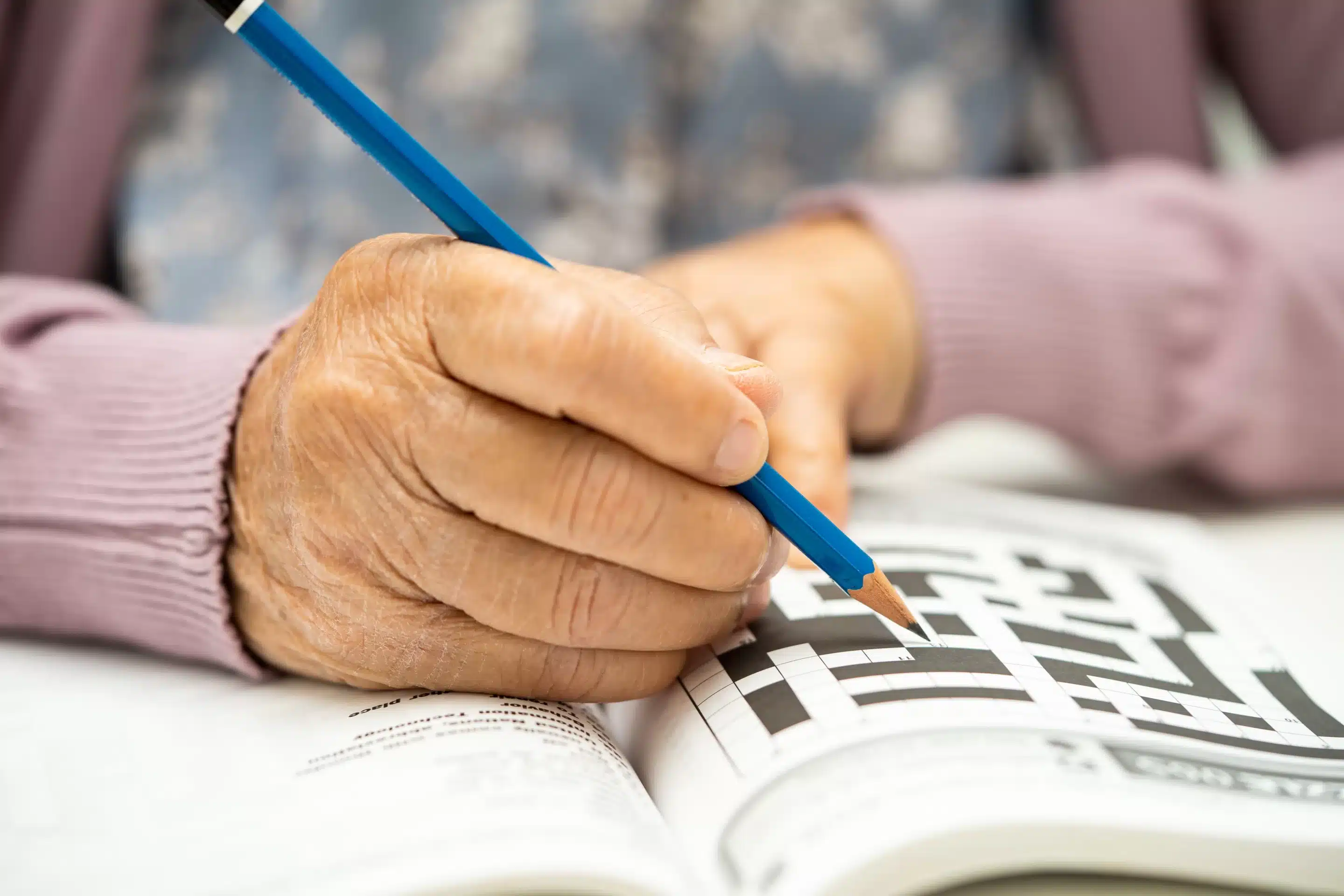 a hand holding a pencil over a crossword puzzle