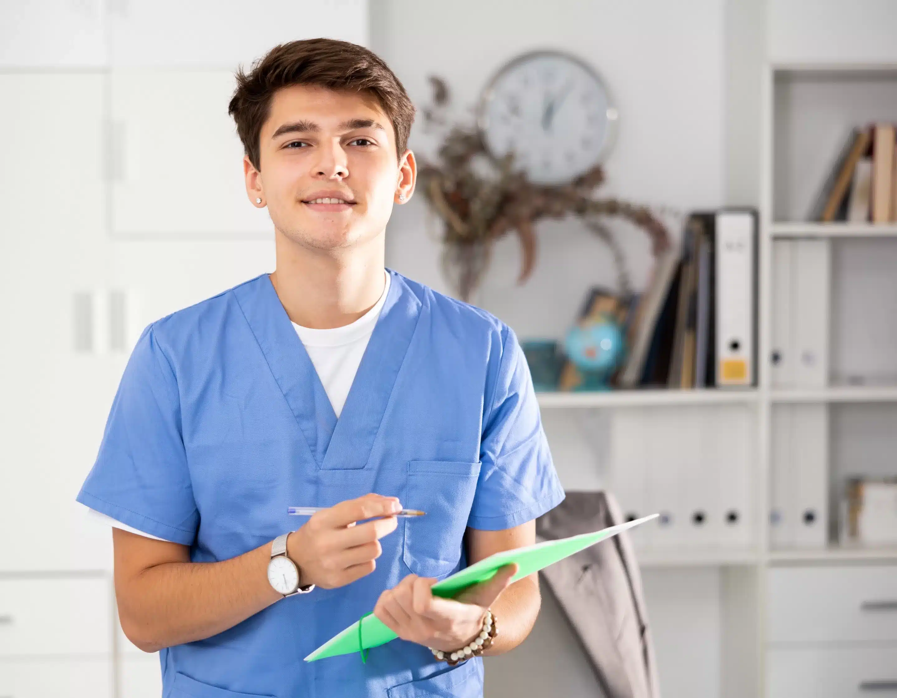a man in blue scrubs holding a clipboard and pen