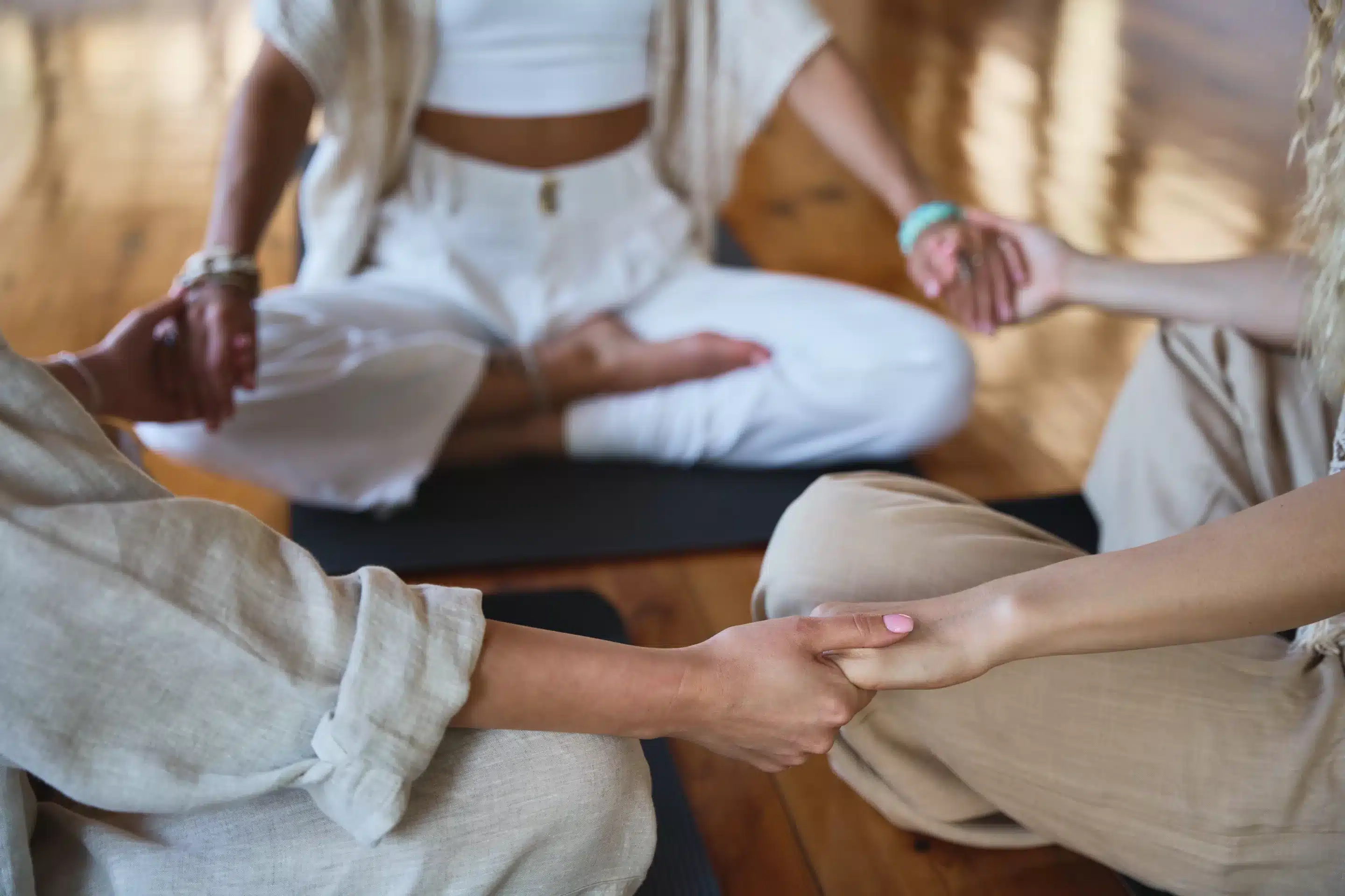 Healthy mindful women group sitting in circle meditating together holding hands