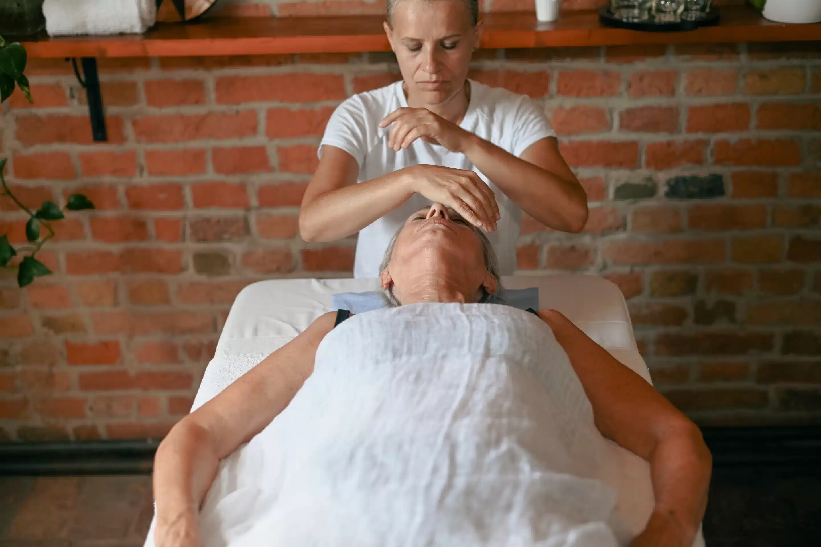 Therapist performing reiki healing treatment, using her hands to channel energy to a patient lying on a massage table