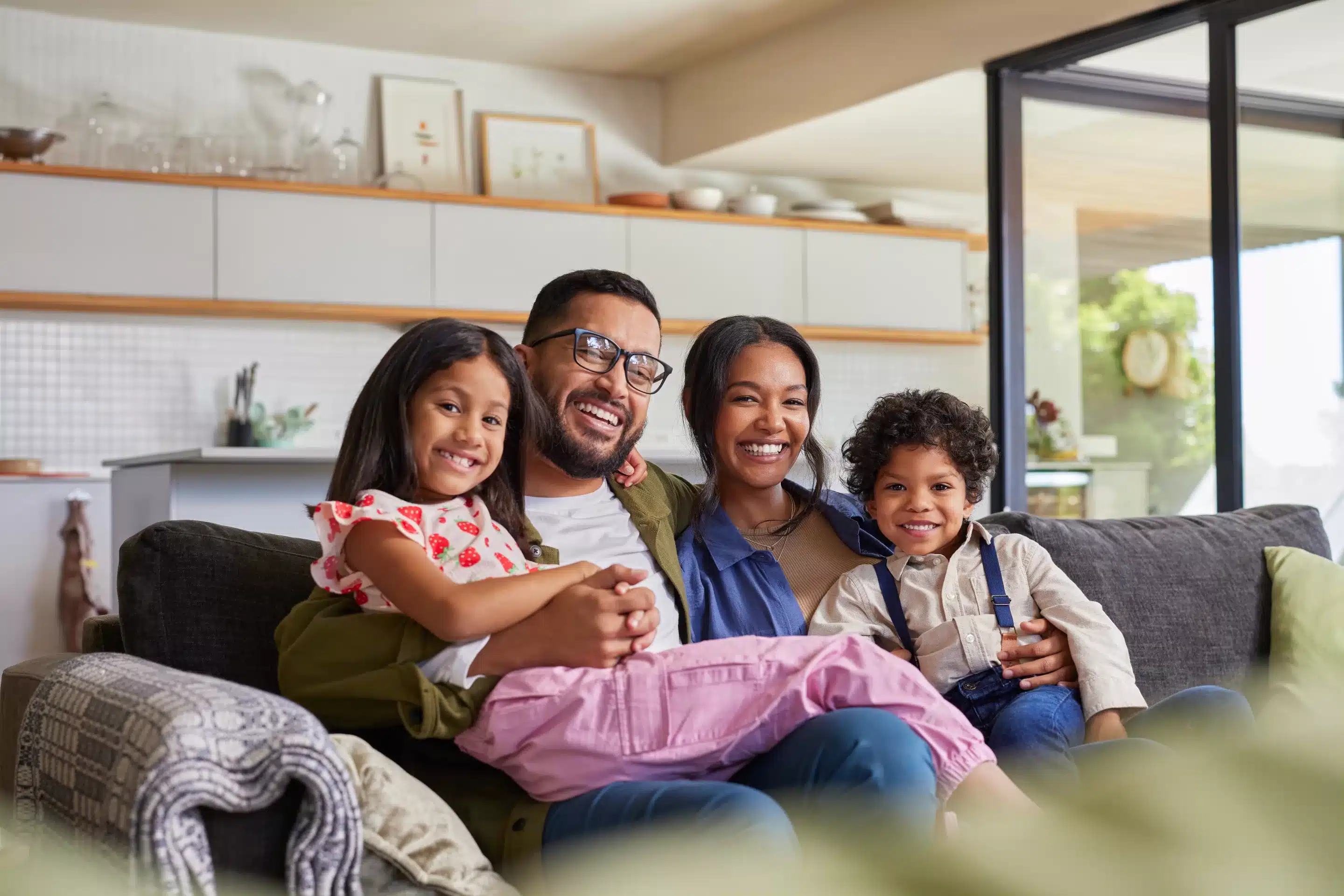 Happy multiethnic family having fun at home, parents and little children sit on sofa together and looking at camera