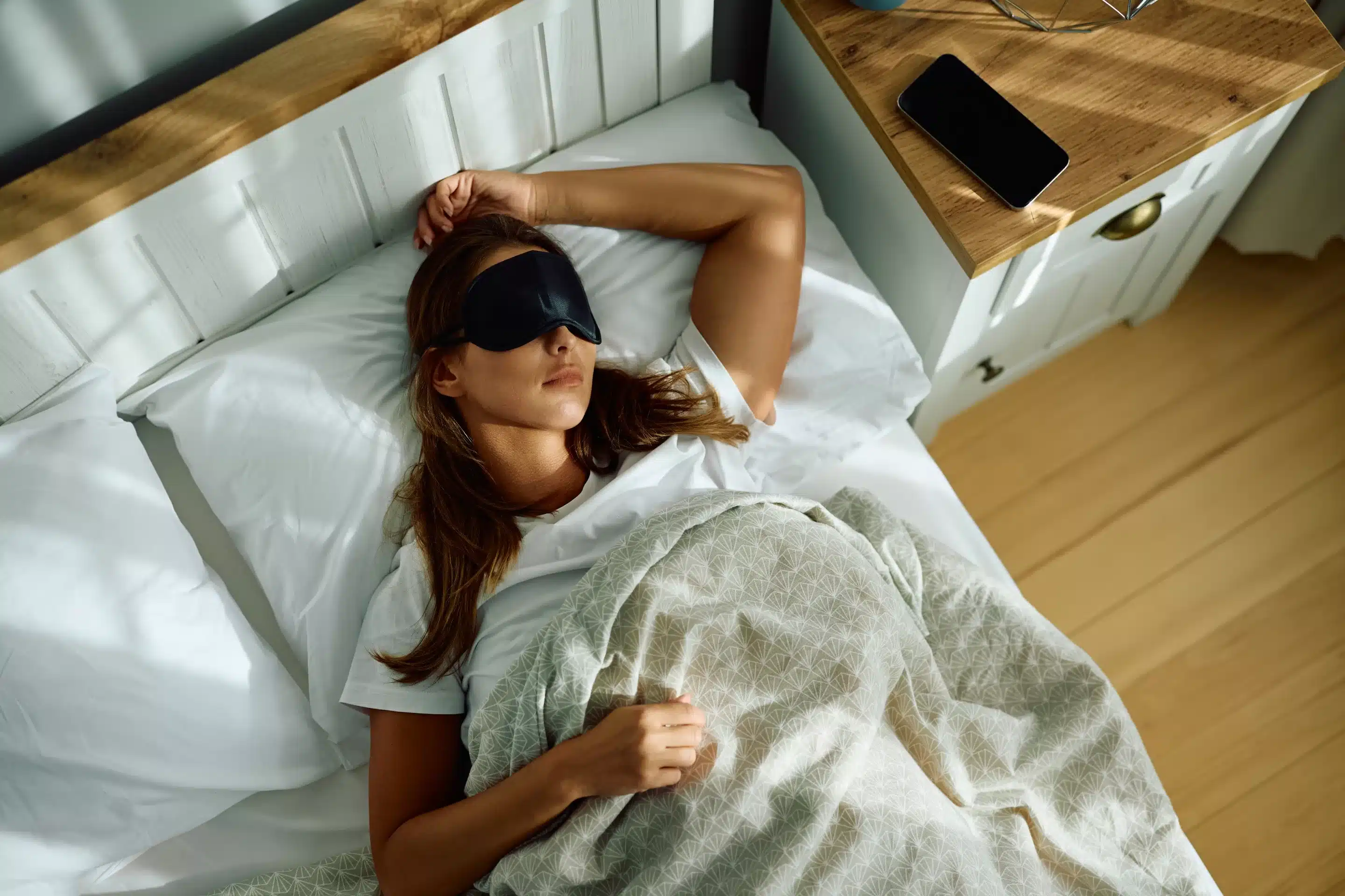 High angle view of woman wearing sleeping eye mask in bed.