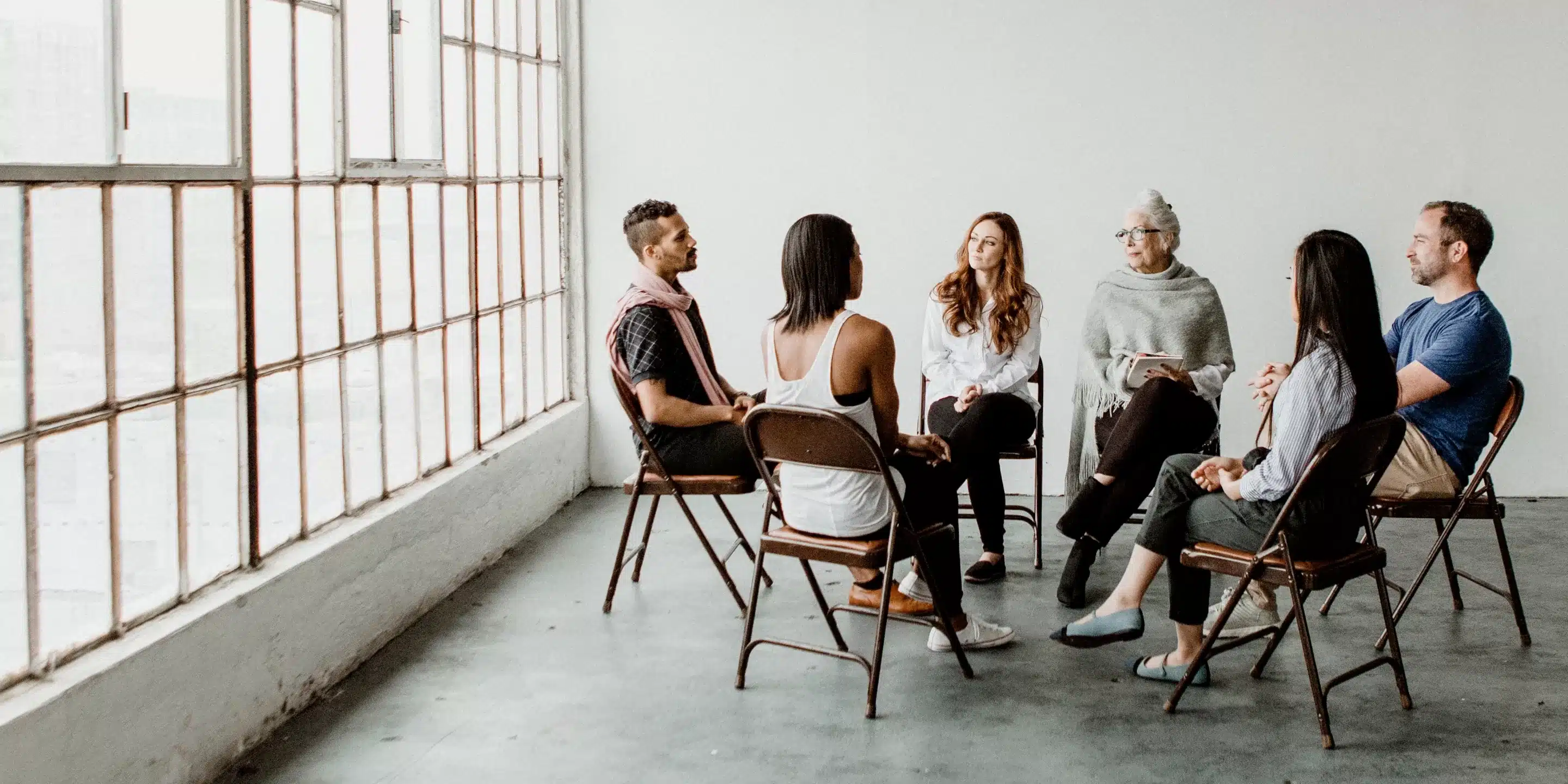 A diverse group of people sitting in a circle, engaged in discussion or group therapy.