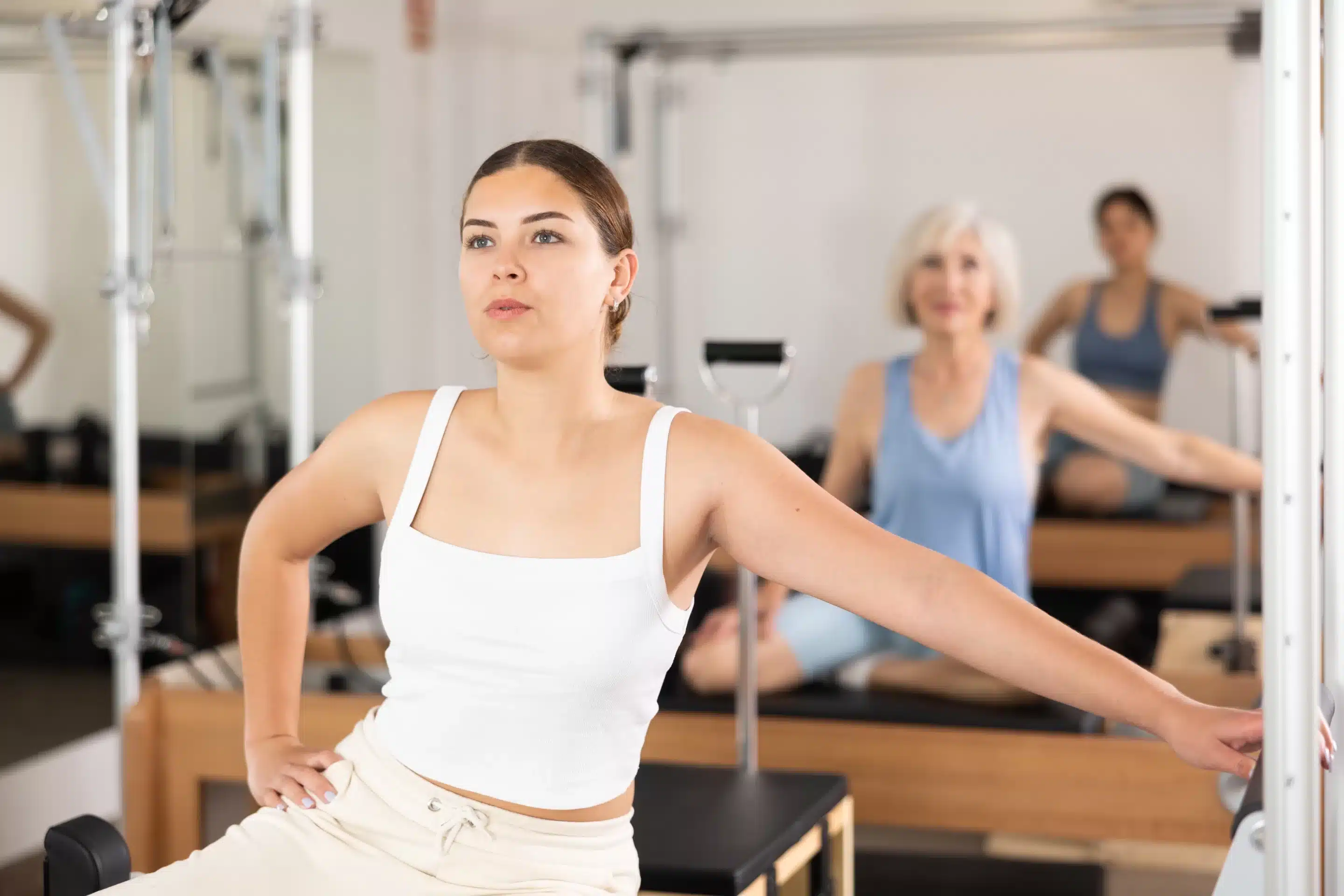 Sporty young girl practicing pilates in fitness studio, doing stretching exercises on reformer.