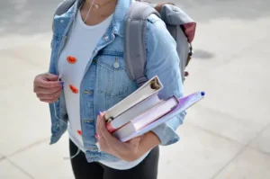 Student girl wearing a backpack, holding three books and a folder, ready for school