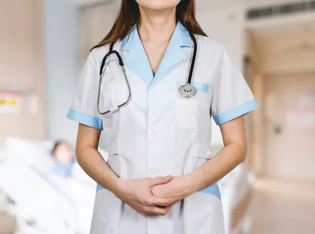 Confident female doctor standing with a stethoscope on her shoulder, wearing a white coat with light blue accents