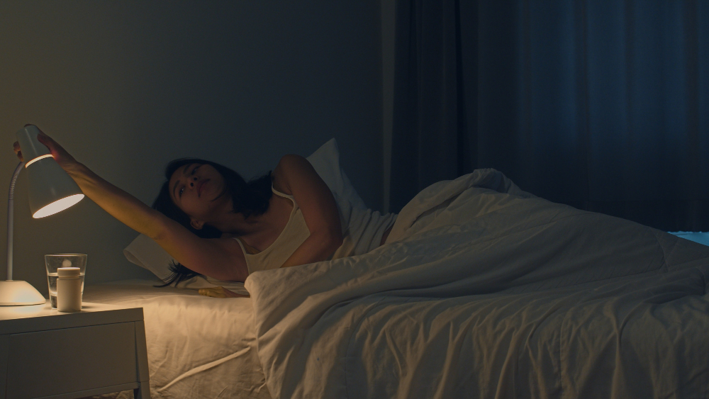Woman turning off bedside lamp before going to sleep in cozy bedroom