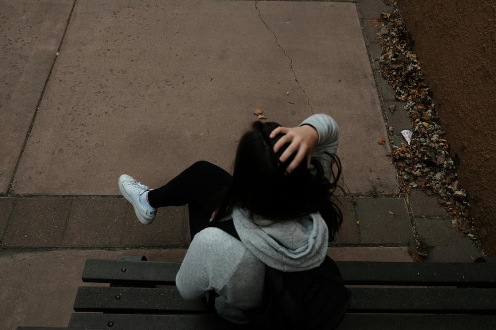 A person sitting on a bench on a sidewalk A person sitting on a bench on a sidewalk