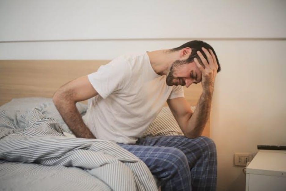 Man sitting on bed, looking distressed.